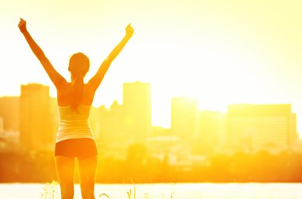 Success winner woman standing with arms up joyful after outdoors workout. Half silhouette on sunny warm summer day with city skyline in background, From Montreal, Quebec, Canada.